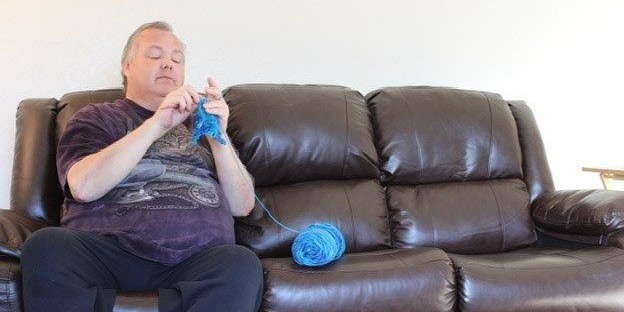 man crocheting on couch
