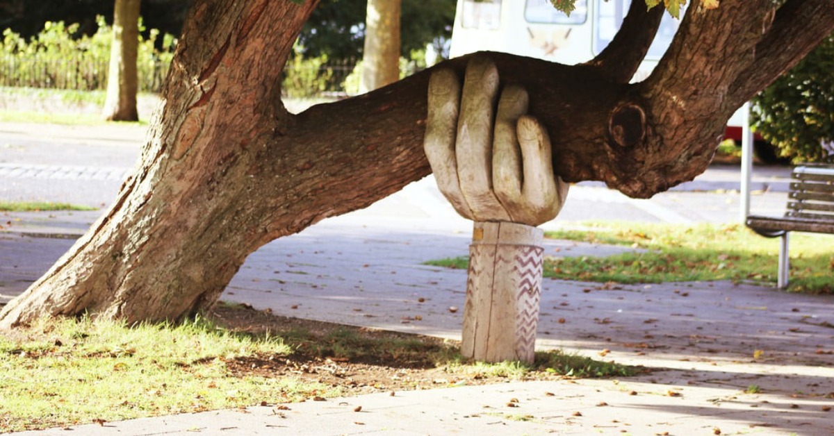 carved wooden hand holding up bending tree