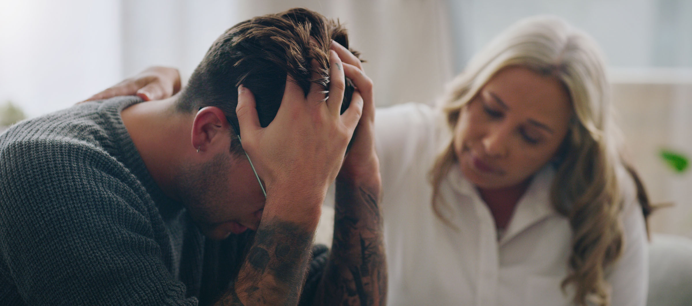 man sitting holding head in his hands while sympathetic woman comforts him
